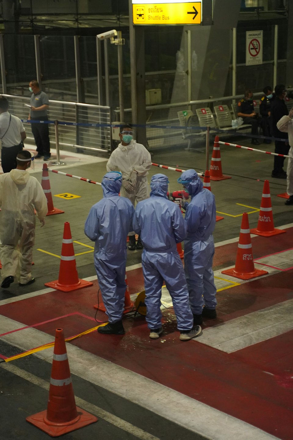 Workers in hazmat suits on a marked floor with safety cones.