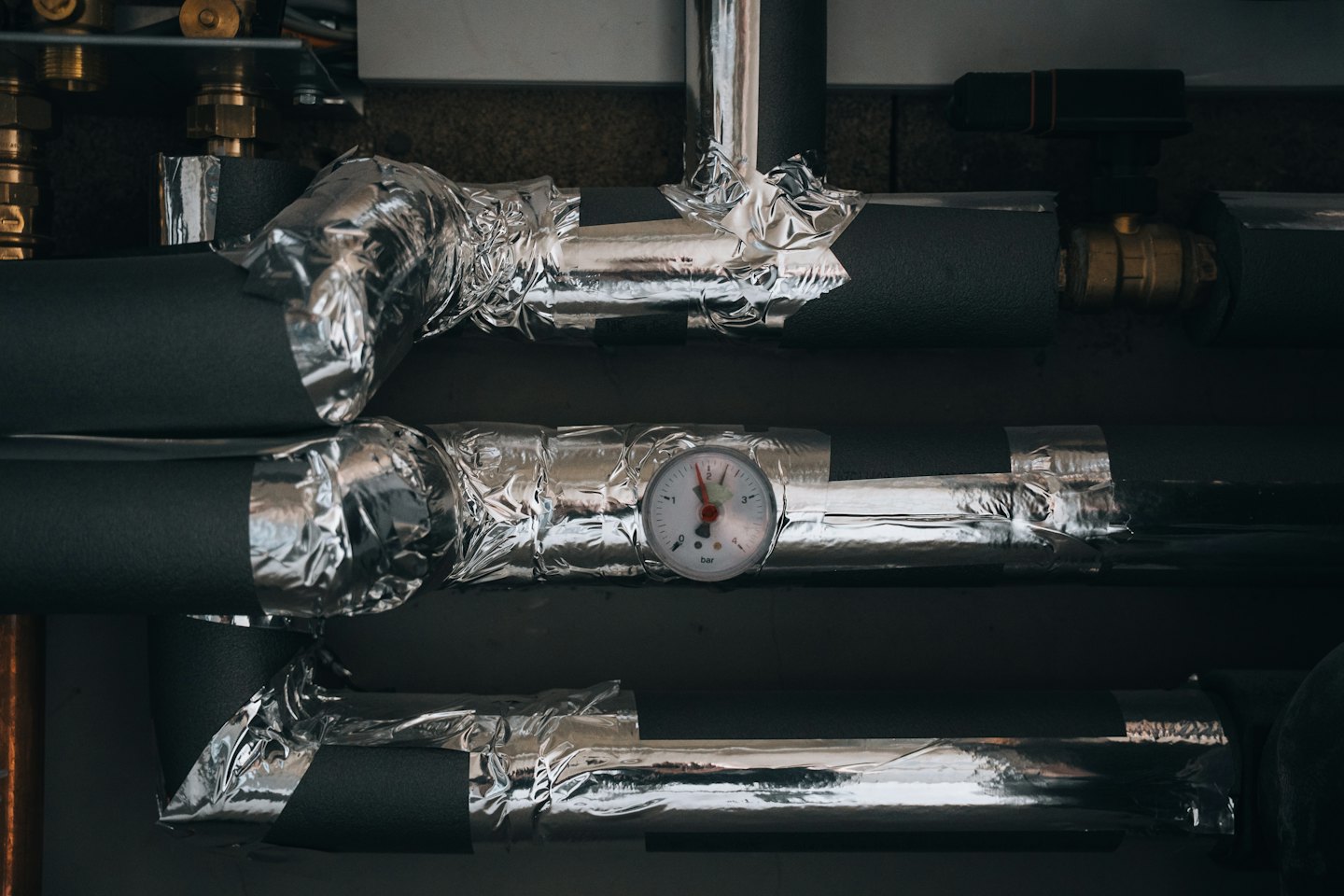 Pipes with insulation and a pressure gauge on an industrial utility system.