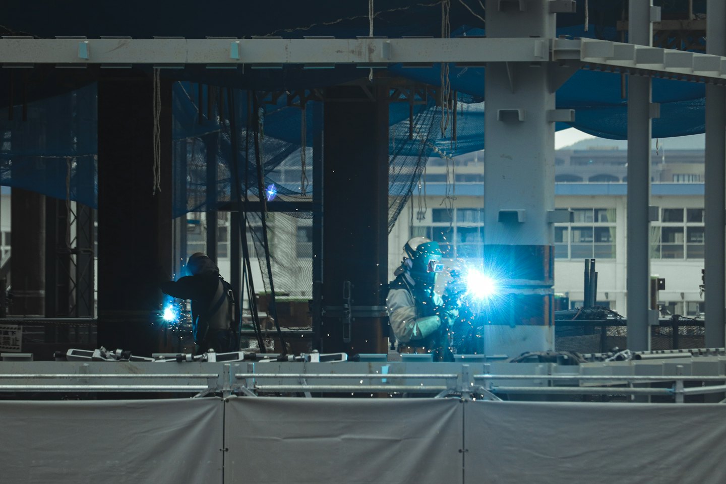 Construction workers weld steel structures with bright blue sparks.
